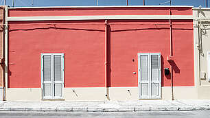 Rot-Braune Häuserzeile in Salice Salentino um die Mittagszeit im Hochsommer, keine Menschenseele und verschlossen Rollladen, Apulien, Italien
